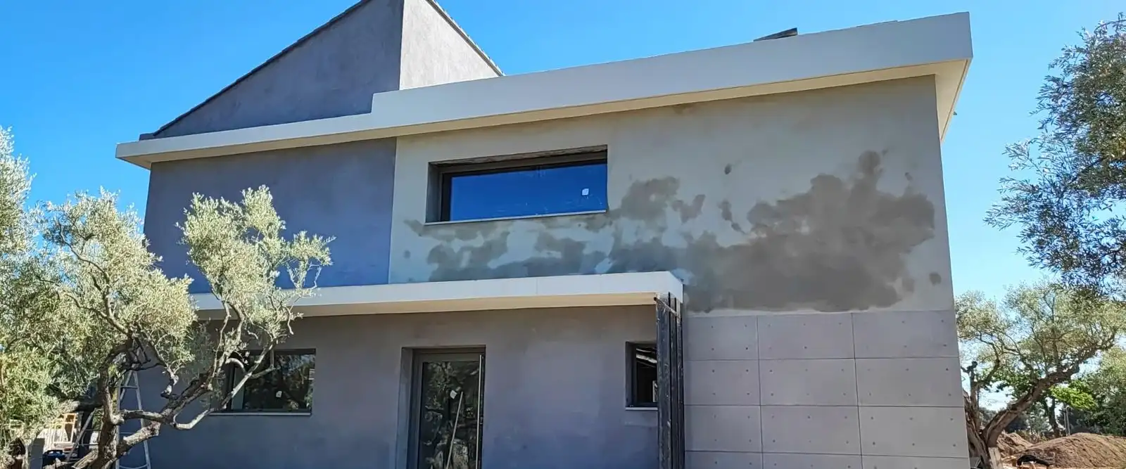 Villa à étage, façade enduite en gris, entourée d’oliviers