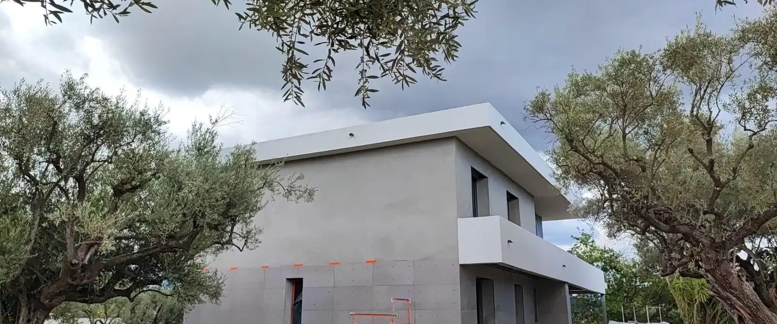 Façade d’une villa neuve enduite en gris, avec des joints creux qui dessinent des panneaux