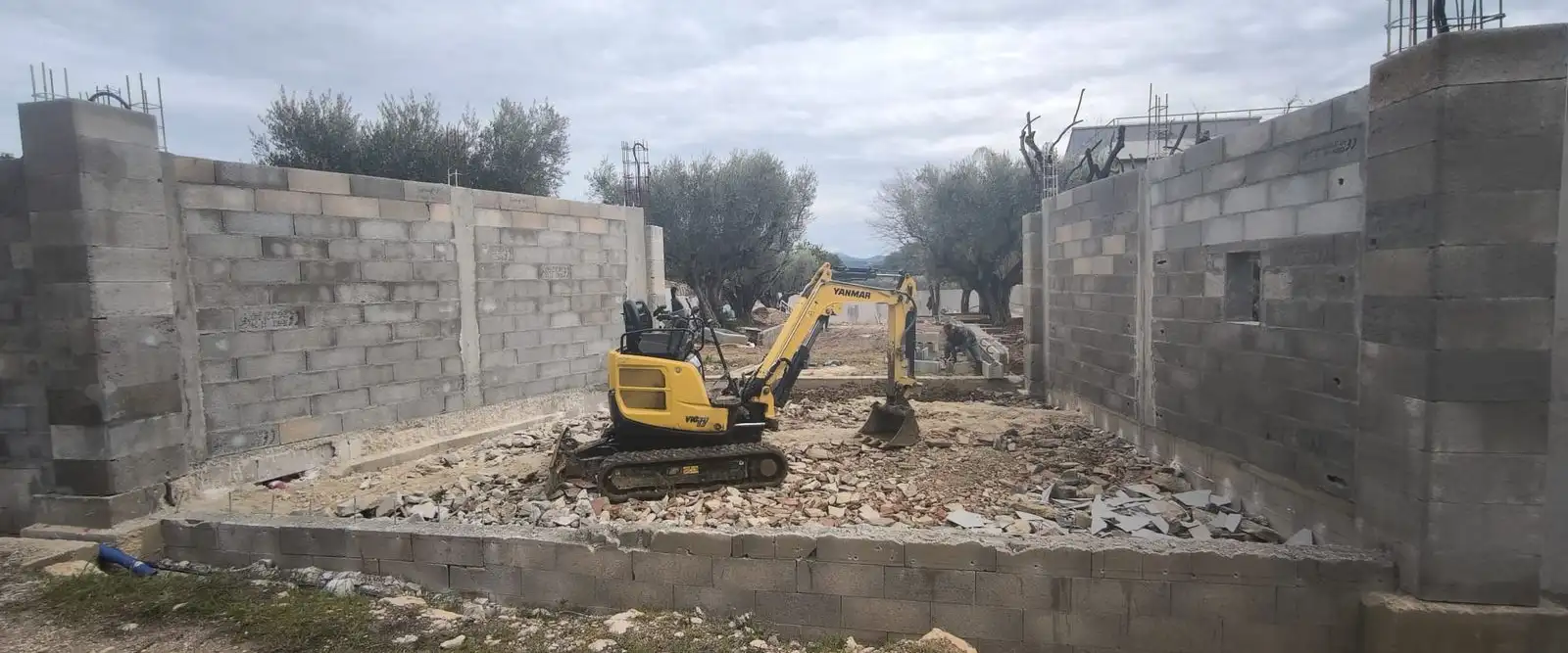 Murs en parpaings montés sur un chantier de gros œuvre, mini-pelle au travail