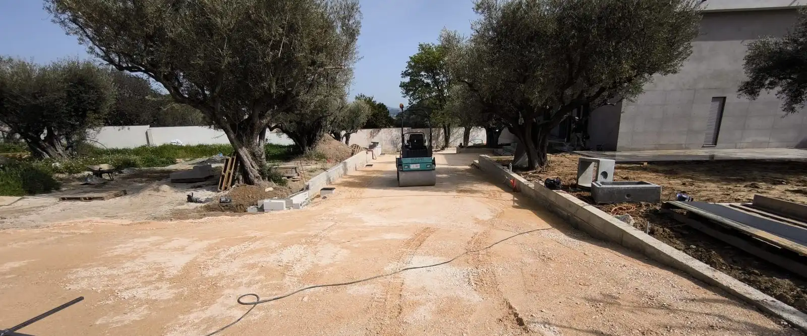 Terrassement de l’accès d’une villa : rouleau compacteur et bordures, entre les oliviers