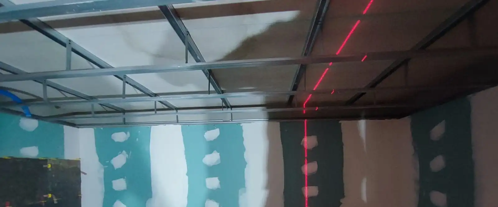 Faux plafond en cours de pose : ossature métallique suspendue, réglée au laser, au-dessus de murs en plaques de plâtre